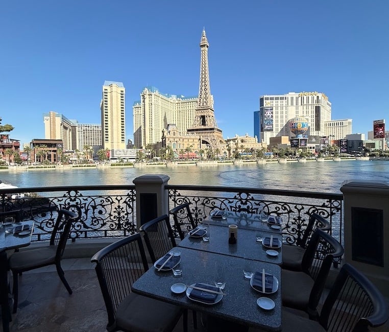 Outdoor dining area on a boat deck overlooking the Las Vegas Strip with Eiffel Tower replica and casino hotels along the water